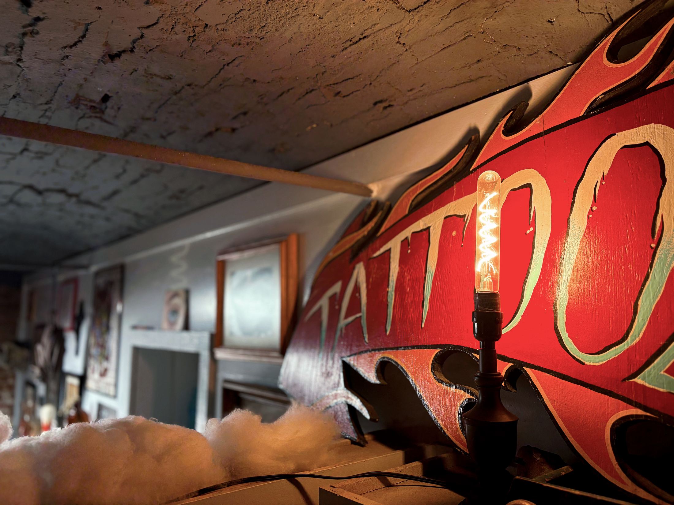 Vintage hand-painted TATTOO sign glowing under a warm Edison bulb inside the studio