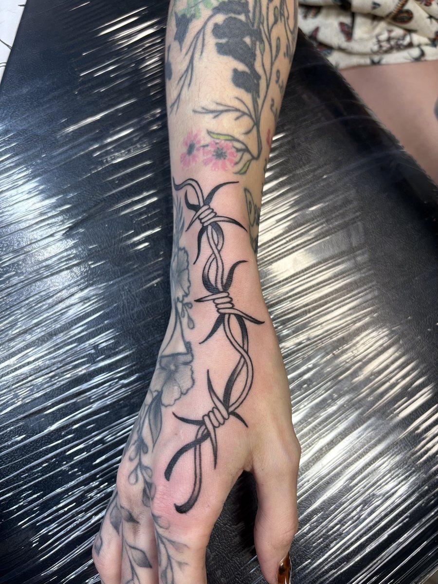 Barbed wire and floral tattoo running down the forearm and hand