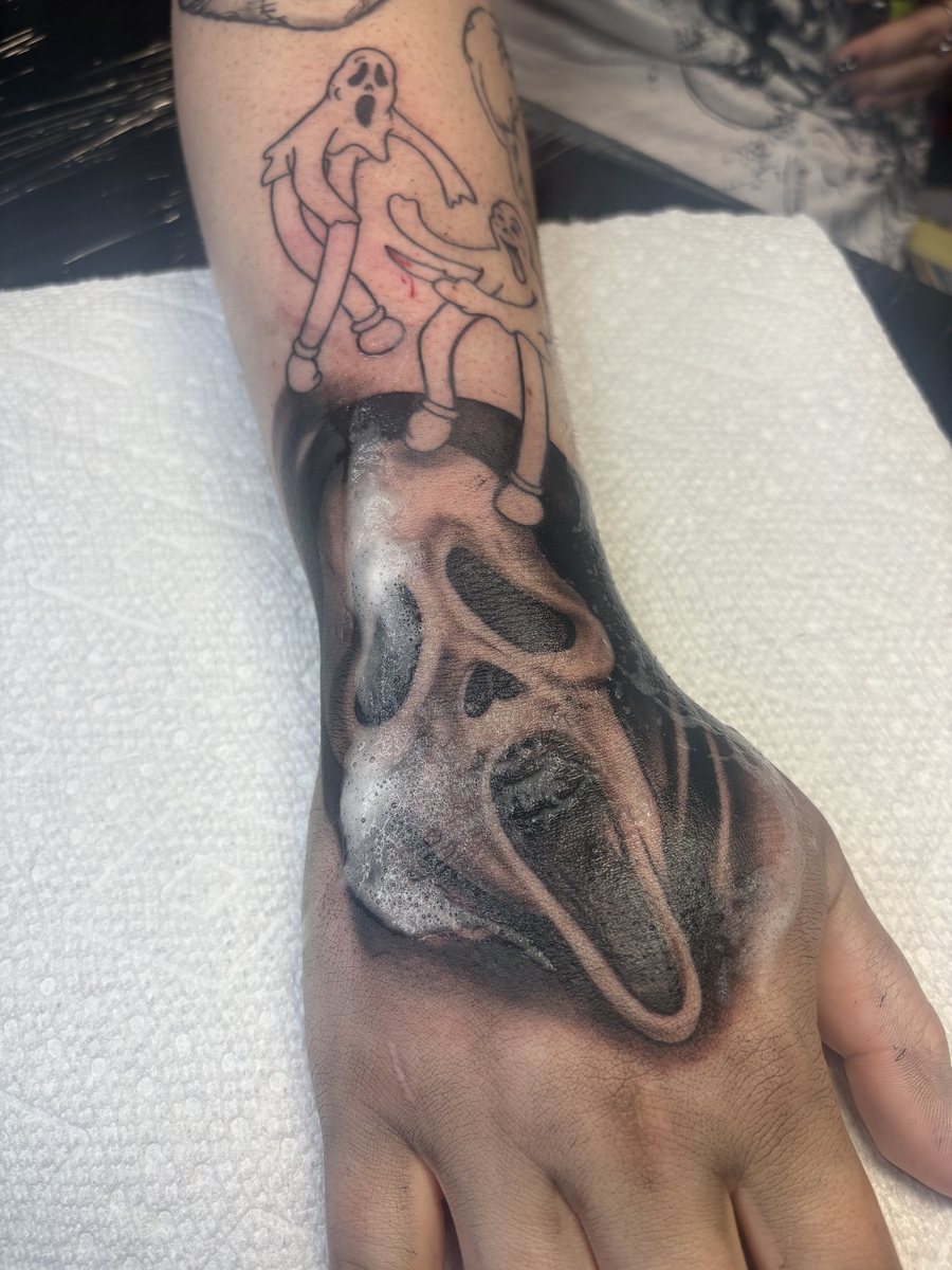 Black and grey realism tattoo of a horror mask on the hand