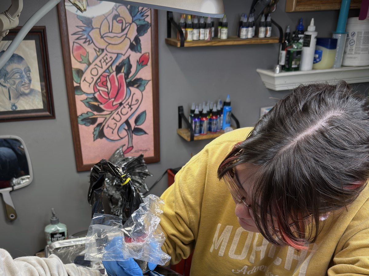 Sam Meyer tattooing a client in her private studio, surrounded by flash art